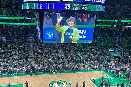 Photo of Regina on the jumbotron at the Boston Celtics after receiving the Heroes Among Us award. She is wearing a jaunty, bright green blazer.