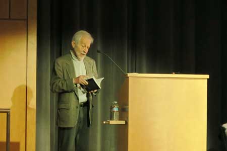 Photo of George Elbaum on stage at SHS with a book in his hand, standing next to a podium