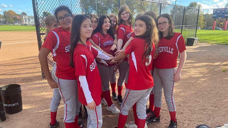 middle grades softball team in a huddle next to field