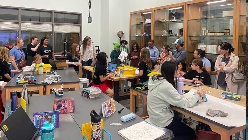 A crowd of students and family members observe a student presentation in the fablab