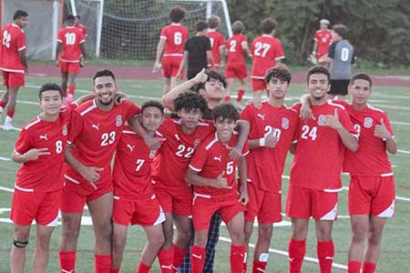 Varsity Boys Soccer team poses in red uniforms on a soccer pitch.