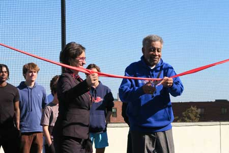 Phil Reavis cuts ribbon at ceremony for field. Mayor Ballantine holds ribbon. Students in background.