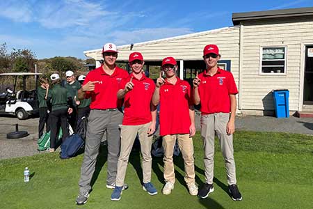 Photo of 4 SHS Golf Team members pointing a finger up to indicate they are number one. They are wearing red collared shirts on the edge of a lawn.