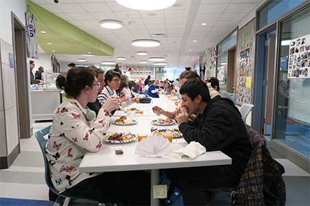 Photo of Students and Staff eating at a long table for the annual Next Wave / Full Circle Thanksgiving dinner, in their new space at the high school.