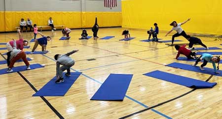 Photo of prekindergarten students practicing yoga in a circle in the East Somerville Community School gym